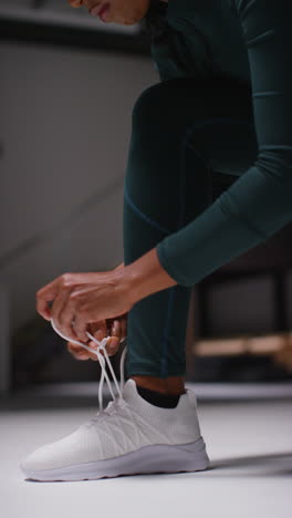 vertical video close up of female athlete in gym or changing room tying laces of training shoe before exercising