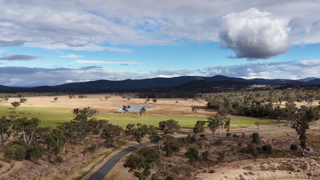 Drone camera glides over a rural landscape with farm ponds, open fields, and scattered trees under partly cloudy skies in Stanthorpe, Queensland
