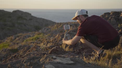 Videographer-filming-with-his-phone-in-beautiful-landscape,-ocean-at-the-background,-sunset,-static-shot