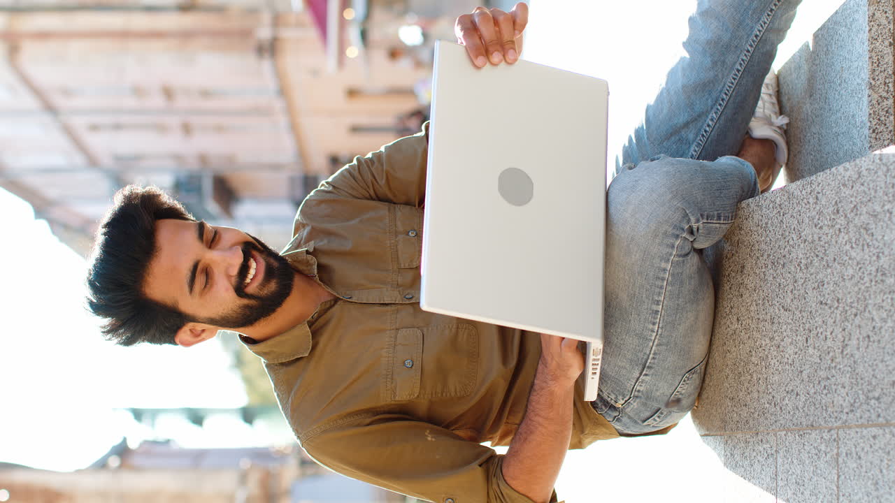 Indian man freelancer sitting in city street opens laptop start working online distant job outdoors