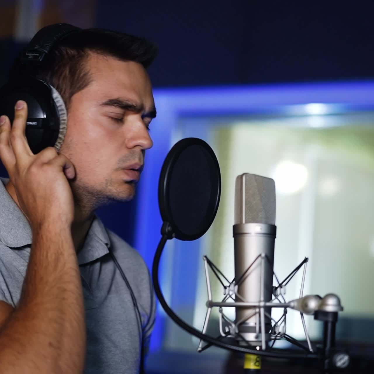 Handsome male wearing headphones singing in studio. Professional singer performing a song, recording music in modern company