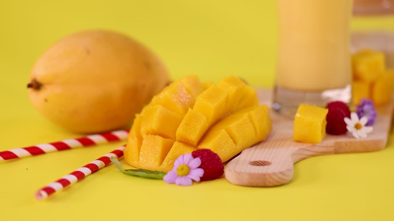 Fresh mango cubes, smoothie, raspberries, and flowers arranged on a cutting board, vibrant lighting