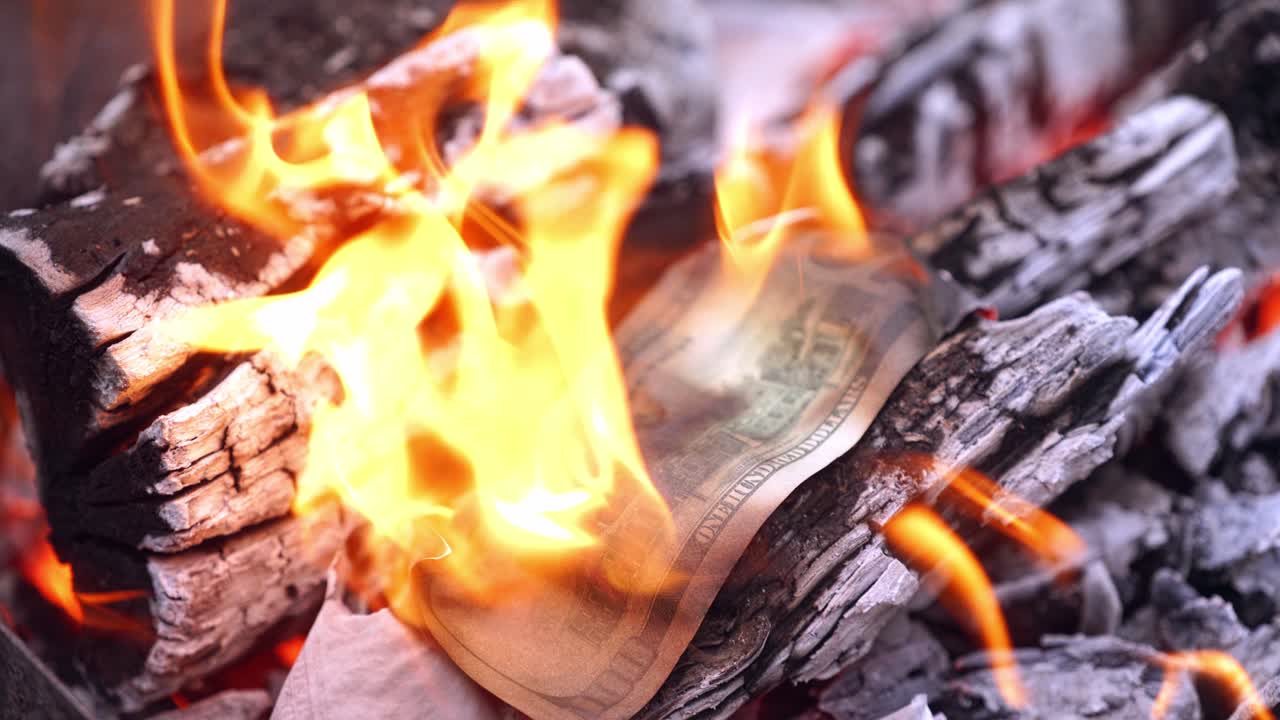 One hundred dollar bill burns in firewood. Someone's hand puts banknote of american money into fire on the background of burning wood. Close-up.