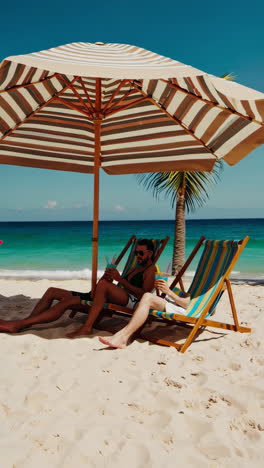 people relaxing and enjoying colorful drinks on a sunny beach under a parasol
