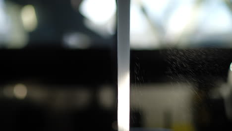 stream of running tap water captured in strong backlight with visible droplets and kitchen background