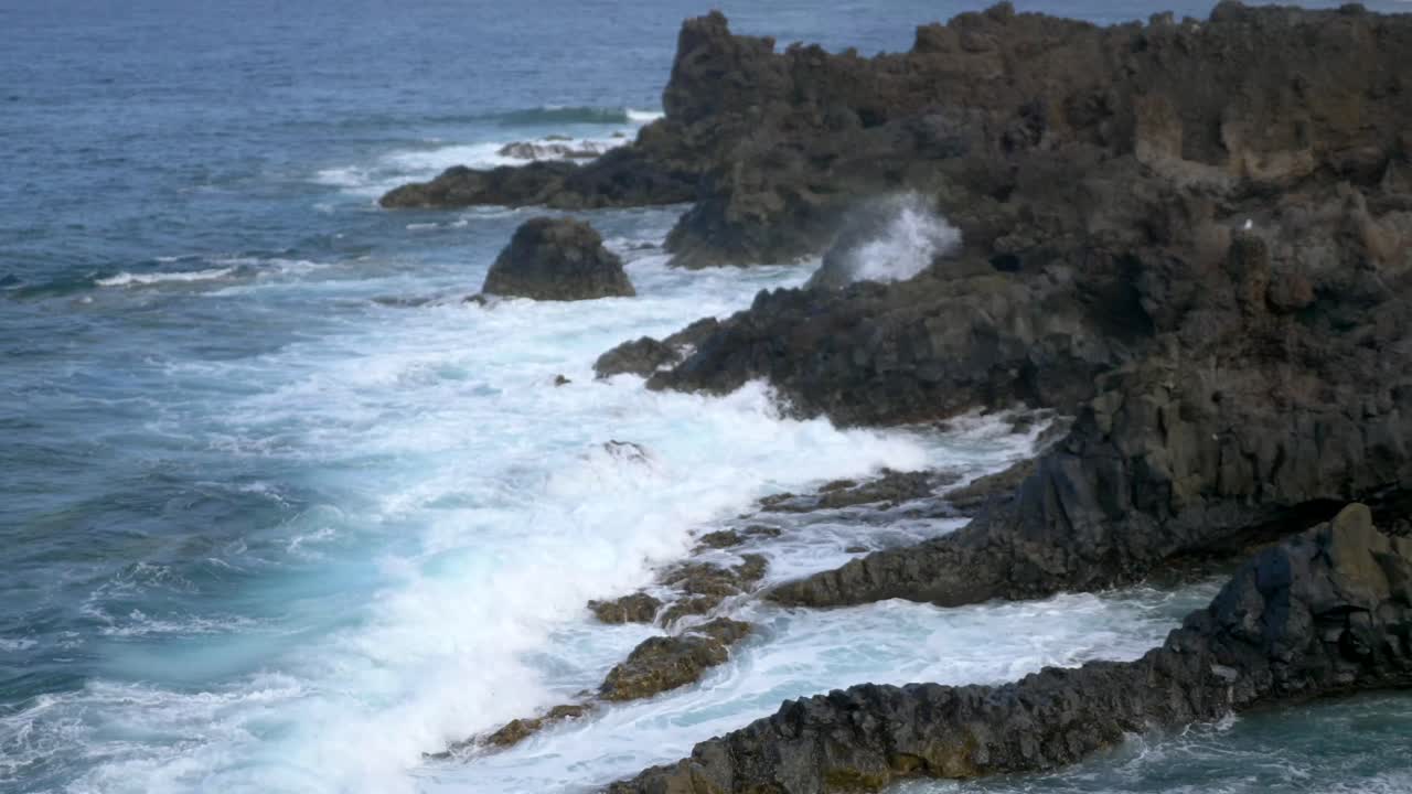 un primer plano de las olas rompiendo y las salpicaduras de agua en la costa rocosa volcánica de lanzarote