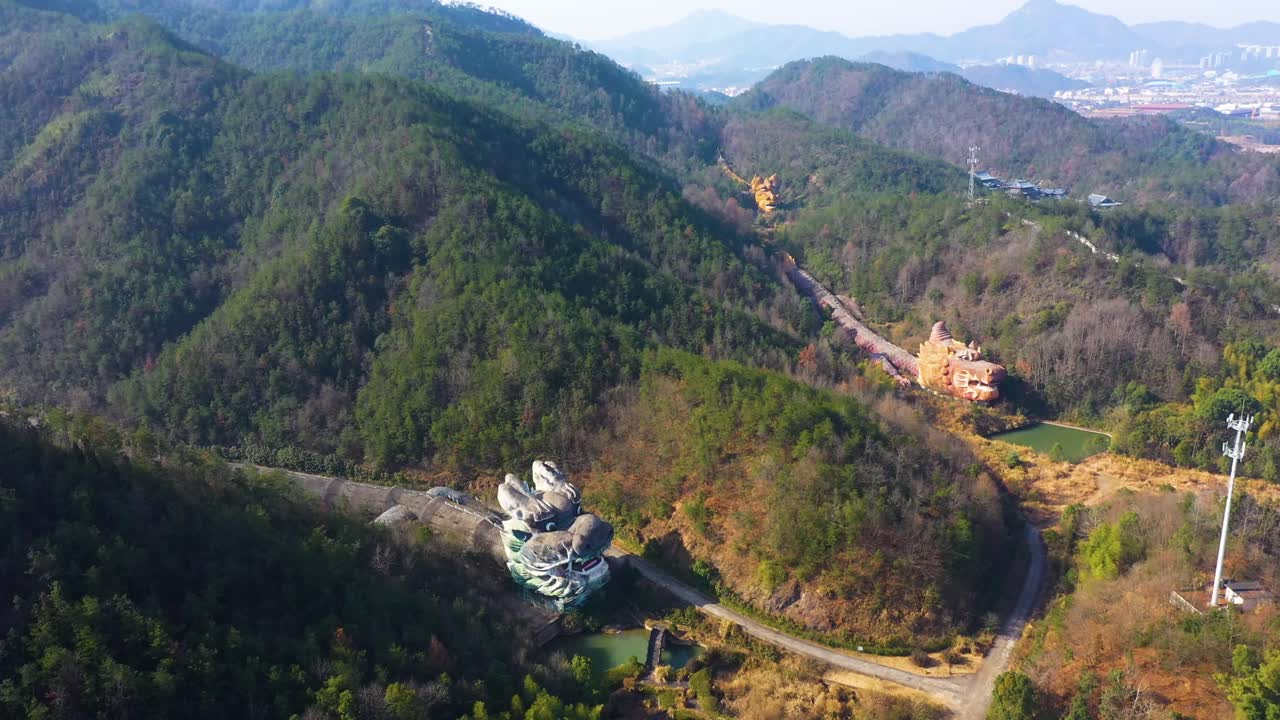 Aerial view of the abandoned Dragon Park in Anhui Province, China, nestled in the lush hills of Jiuhua Mountain. The eerie yet captivating structures are surrounded by dense forest and natural beauty.