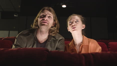 front view of concentrated couple sitting in the cinema while they watching a movie and talking