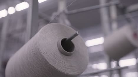 close up shot of high tech machinery in factory weaving material on reels of thread