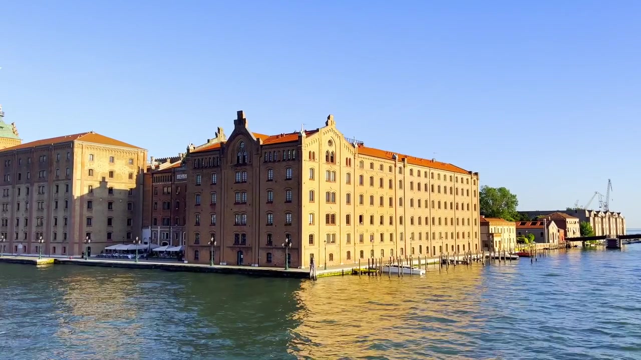 Passando l'edificio del Molino Stucky sull'isola della Giudecca a Venezia, Italia. Un filmato grandangolare mostra la storica struttura sul lungomare riflessa nella laguna in condizioni pomeridiane