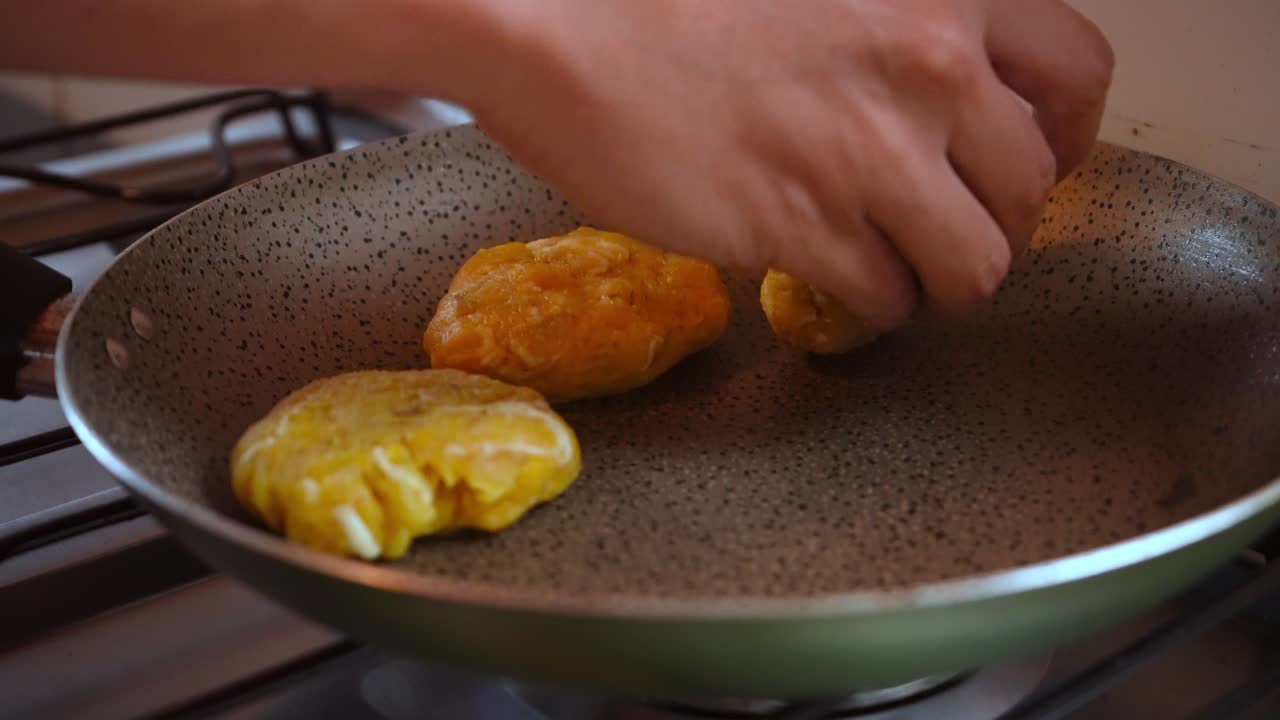 Close-up of a hand placing ripe plantain and cheese patties on a hot nonstick pan. Homemade Latin American cooking. Great for recipe content or food ads.