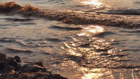 Wellen,-Die-An-Die-Küste-Fließen,-Reihen-Sich-Bei-Sonnenuntergang-An-Die-Felsen,-Während-Das-Sonnenlicht-Auf-Dem-Wasser-Glitzert