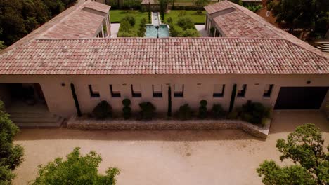 aerial view of a provençal roman-style villa with a courtyard, pool, and garden, revealing an olive grove through a tilted drone shot