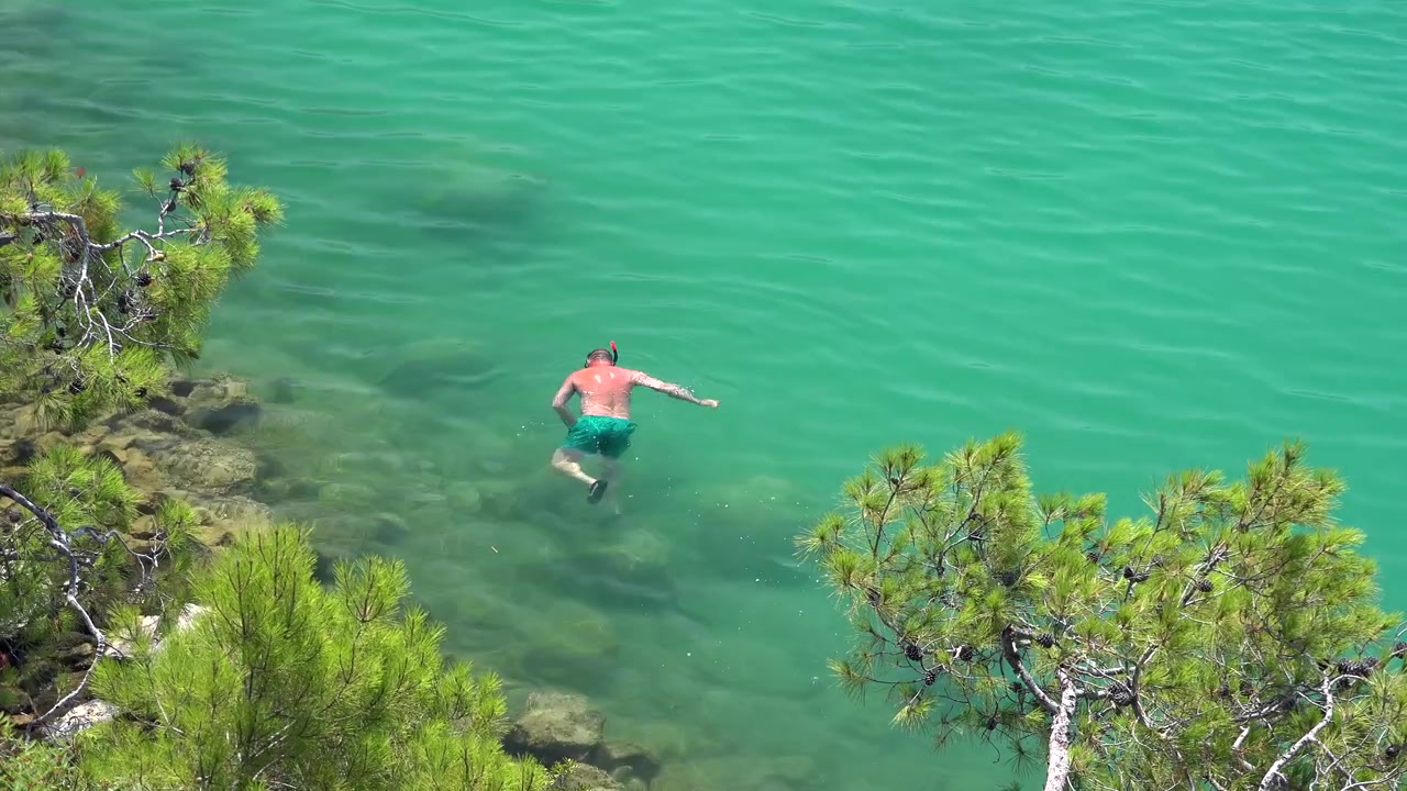 Uomo che fa snorkeling in acqua limpida e turchese vicino a una costa rocciosa.