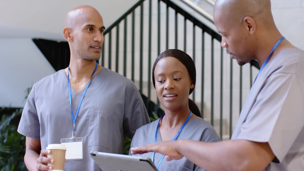 Tre membri dello staff in divisa chirurgica ai gradini della clinica, una donna guida la revisione al tablet mentre un collega a sinistra digita tenendo una tazza