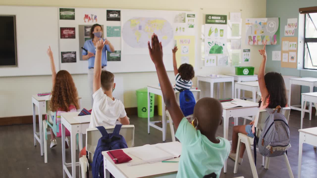 Group of kids raising their hands in the class at school