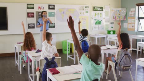 Grupo-De-Niños-Levantando-La-Mano-En-La-Clase-En-La-Escuela