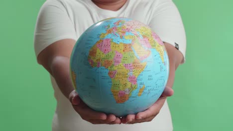 a man in front of green screen background hand in the world globe to the camera