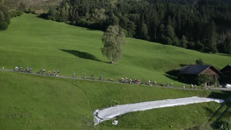 drone shot capturing cyclists pedaling past traditional mountain houses in the scenic tyrolean alps.