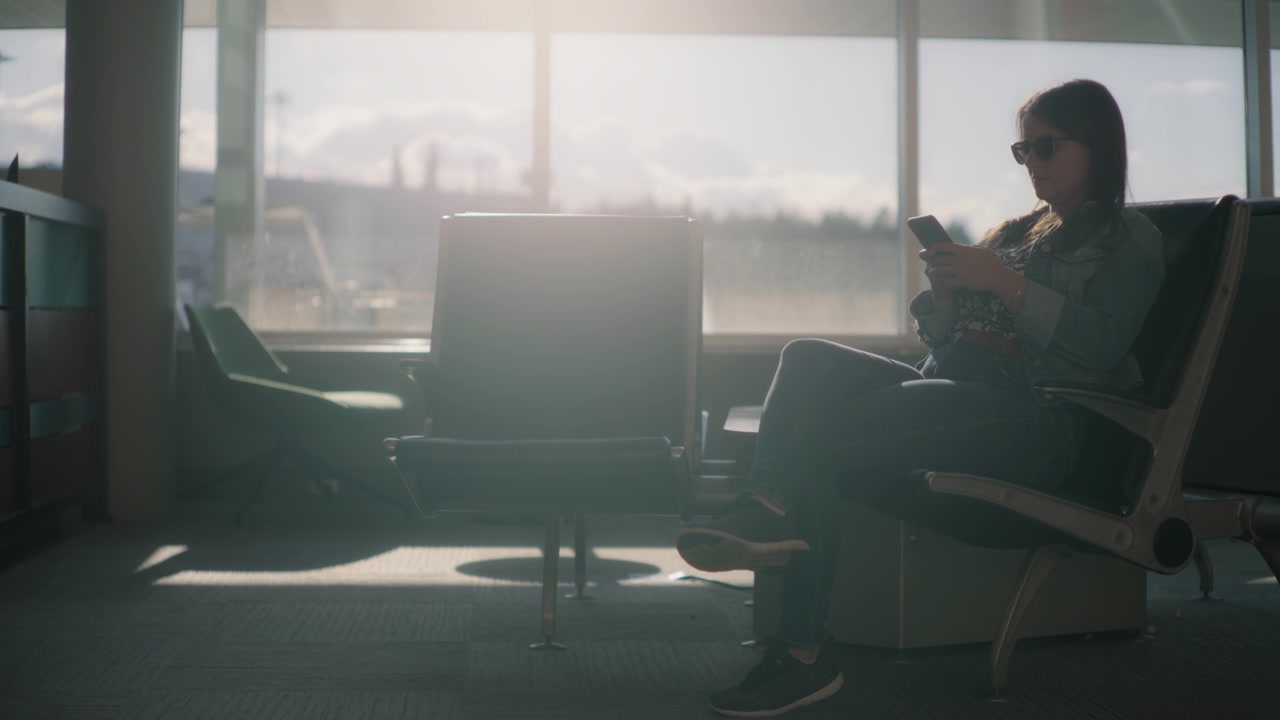 A young woman using her phone while sitting in the airport terminal