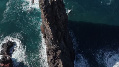 Majestic-black-volcanic-rocks-in-beautiful-blue-ocean-with-waves-crashing-in-creating-foam-during-sunny-day