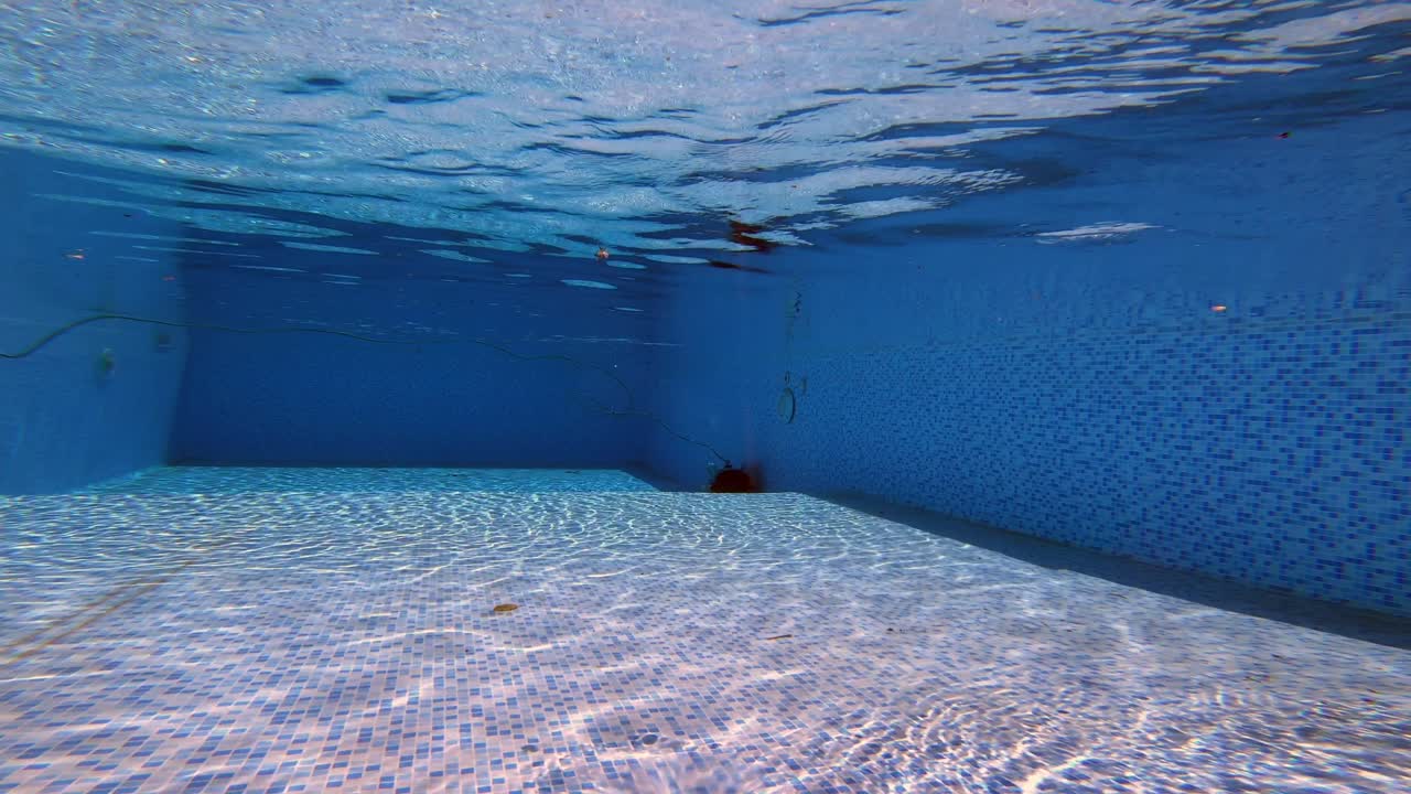 A robotic pool cleaner glides along the wall of a swimming pool under clear blue water. Captured in natural sunlight, showcasing efficient smart technology for pool maintenance.