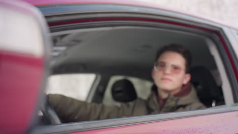 freelancer inside vehicle rolls down car window during cold winter day as snowflakes fall and scatter across glass surface with faint reflection of driver in background