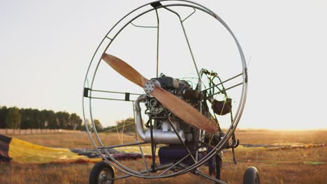 the motor paraglider stands in the field at sunset with a wooden propeller, and the pilot lays out the parachute and aligns the slings. flight preparation