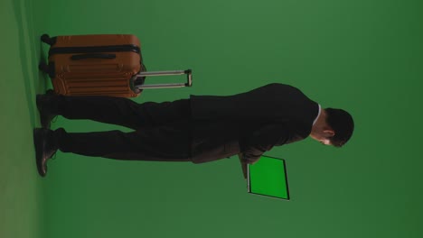 full body of back view asian businessman traveler with luggage use green screen laptop while standing in the green screen background studio, during sunset time