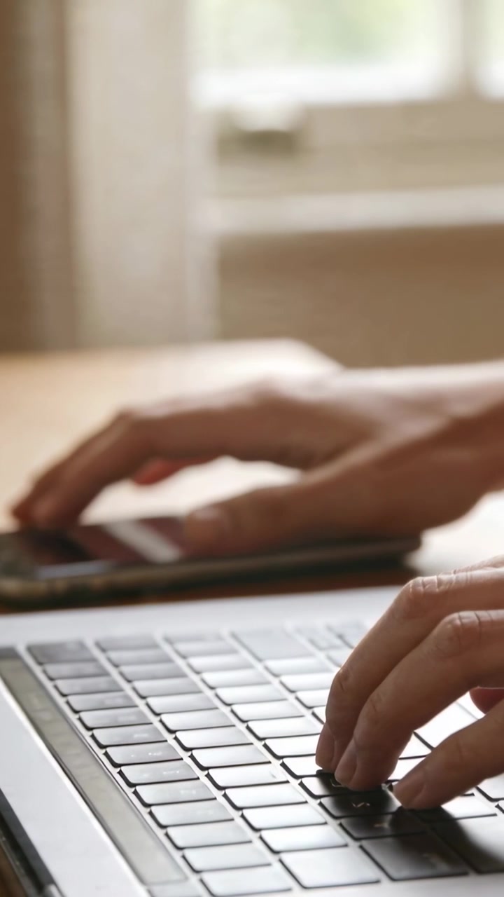 Video verticale: Mani che digitano, braccia nude che si fermano alla scrivania, toccano il telefono, poi riprendono a digitare sul puntatore rosso del laptop.