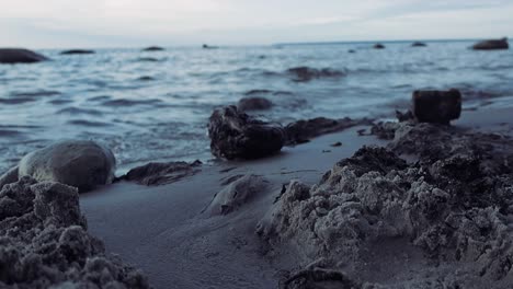 close up footage of a sandy beach during sunset or dusk while the waves are visible in slow motion in the background, ocean sea water with rocks and sandy piles visible with horizon in 4k resolution