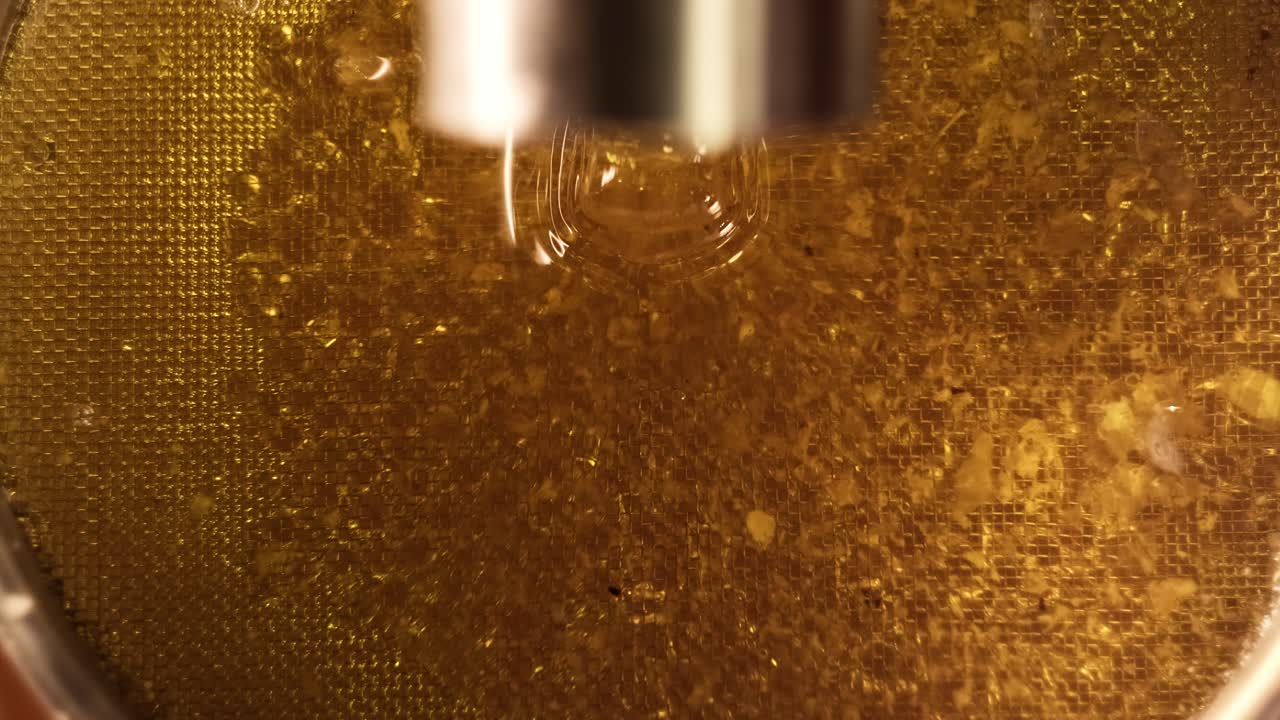 Primo piano di miele biologico in fase di estrazione, processo di raccolta in apiario.