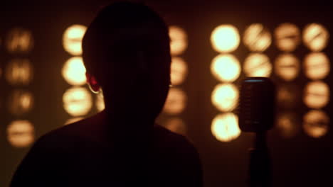 unrecognizable man singing microphone in night club. silhouette of guy singer.