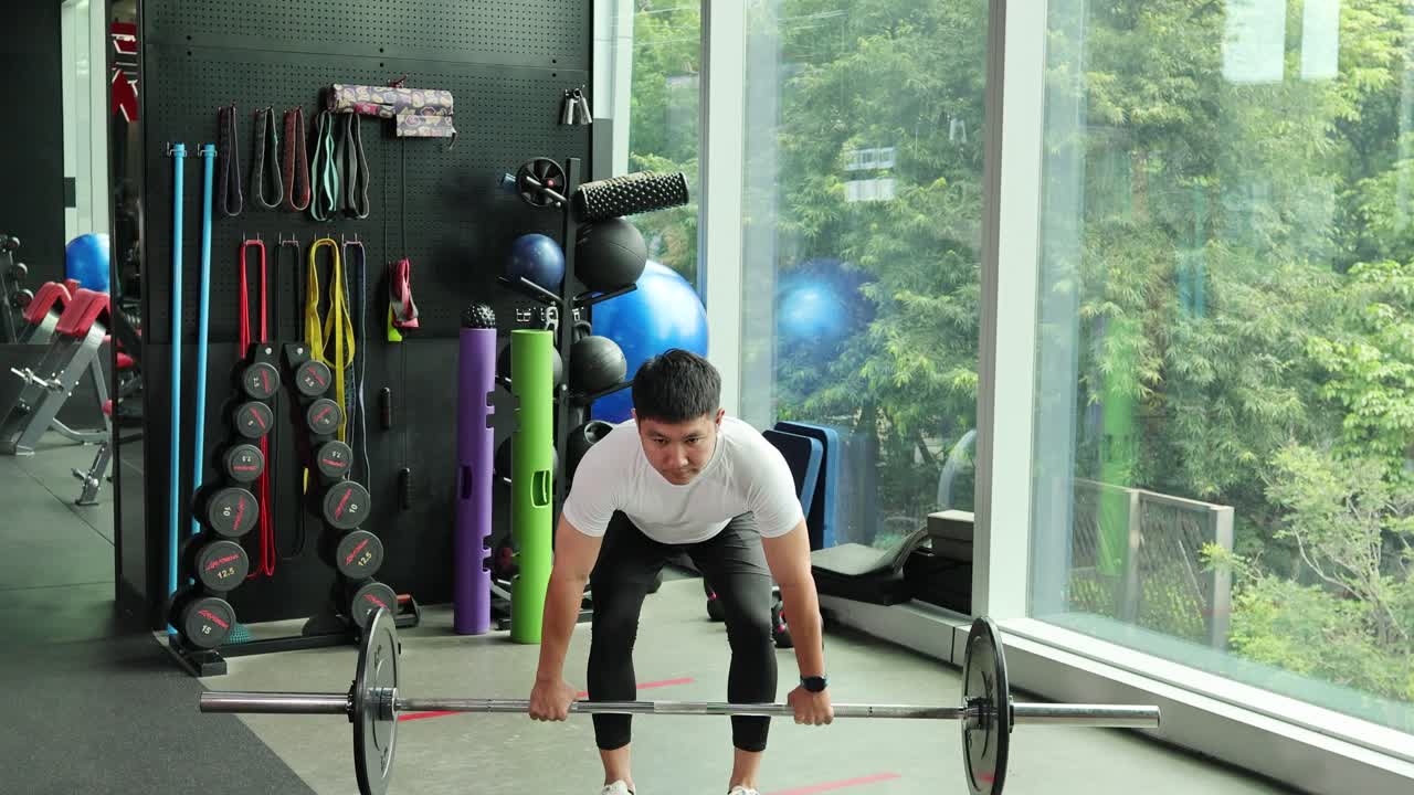 A man in a gym executes barbell deadlifts with natural lighting and a view of greenery
