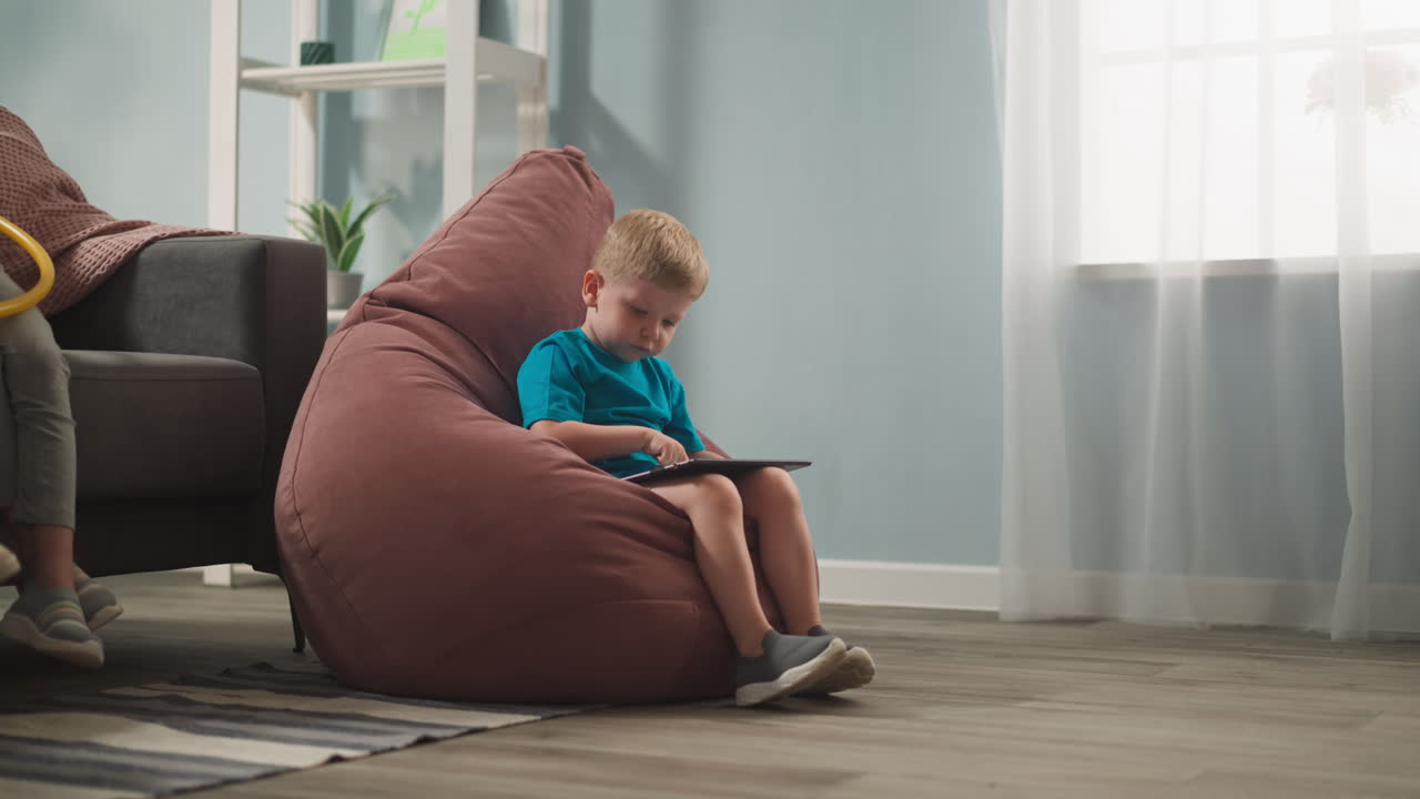 Adorabile bambino gioca a un videogioco seduto su una poltrona a sacco.