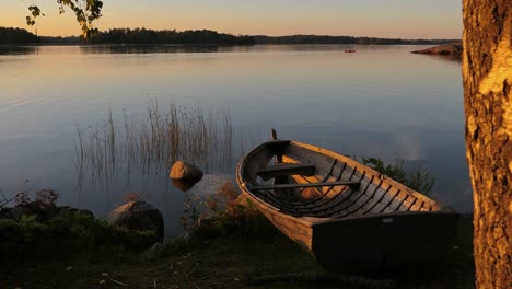 Sunset-calm-water-sea-and-rustic-wooden-boat-at-golden-hour,-reveal-shot