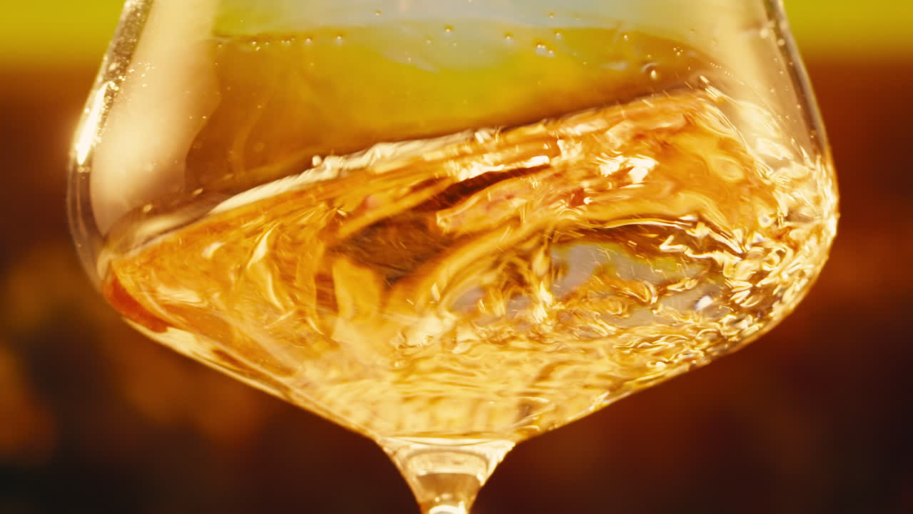 Orange or white wine bottle and glass against a sunset in a peaceful vineyard, pouring of ecological natural wine.