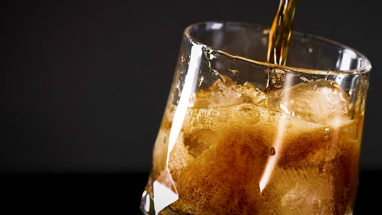 A detailed view of cola being poured into a glass filled with ice, highlighting the fizz and bubbles.