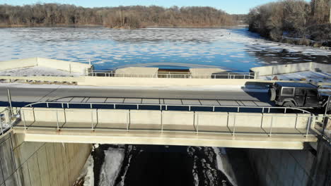 aerial video lowering below a bridge to view a flowing spillway from a frozen man made lake in winter