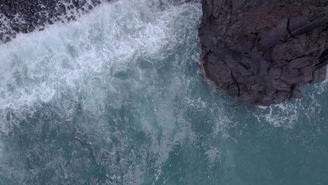 Aerial-close-top-down-shot-of-the-sea-waves-crashing-on-the-volcanic-cliffs-of-Sicily,-Italy