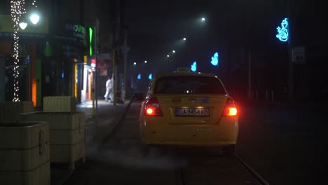 taxi cab idles outside of empty restaurant and shops at night time