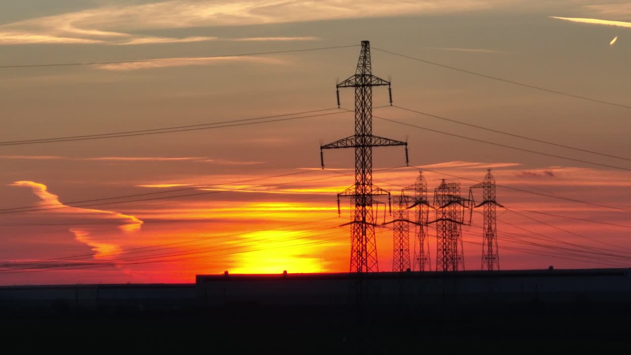 plano general aéreo que muestra torres eléctricas industriales frente a la puesta de sol dorada
