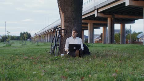 young man working on laptop outdoors under a bridge