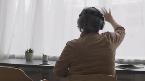 senior woman using virtual reality headset glasses and moving her hands while sitting on chair in a modern living room 3