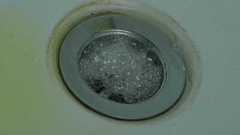 soap foam and water swirling in sink drain hole - high angle, close up