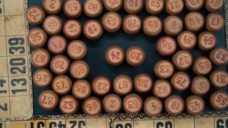 primer plano cinematográfico suave disparo desde arriba de una pila de barriles de madera de bingo en un cuadrado, figuras de madera, viejos números de fondo, juego de mesa vintage, cámara lenta 120 fps comercial zoom out video gimbal