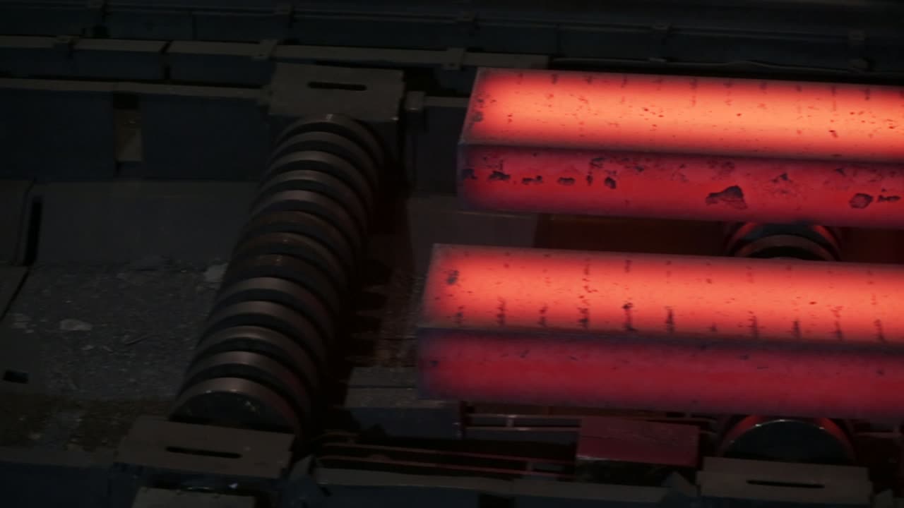 어두운 산업 환경에서 컨베이어 벨트에 반이는 은 뜨거운 강철 막대기