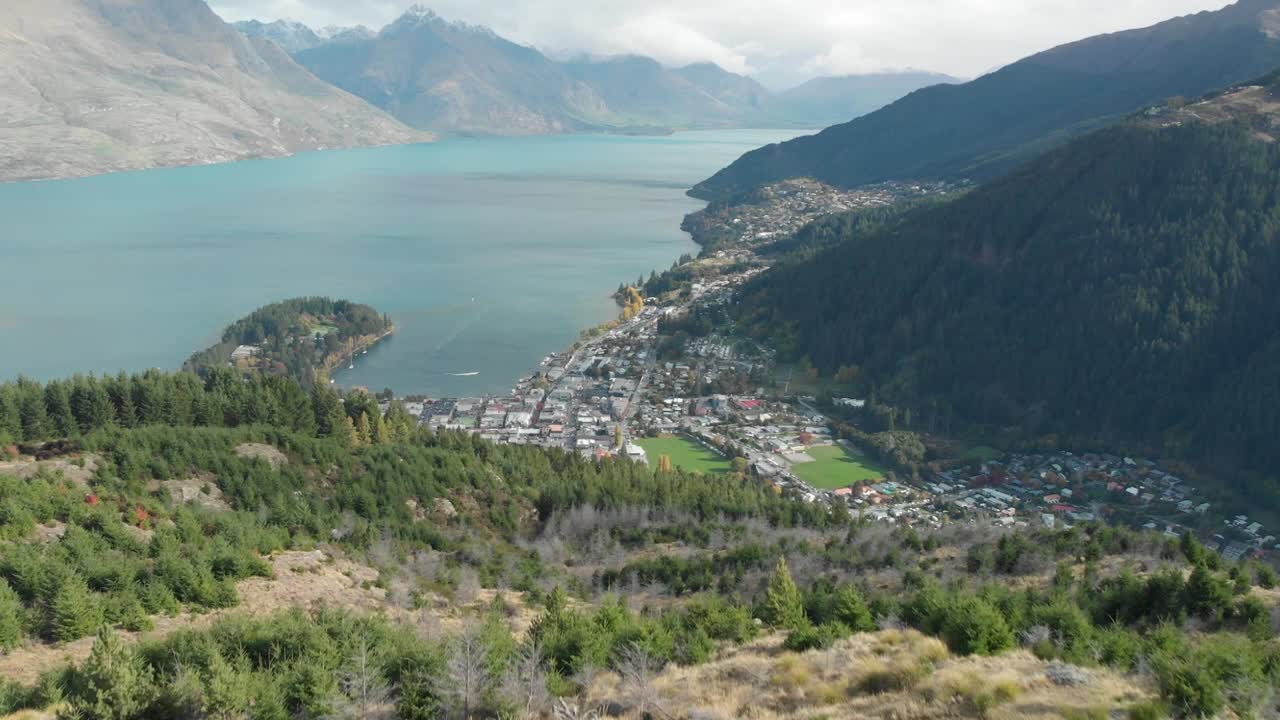 SLOWMO - Queenstown Hill track hike, New Zealand and Lake Wakatipu, mountains with fresh snow, clouds and town - Aerial Drone