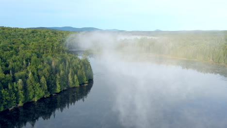 aerial drone shot flying through thick fog and mist hanging over the water of spectacle pond in the forest of the maine wilderness