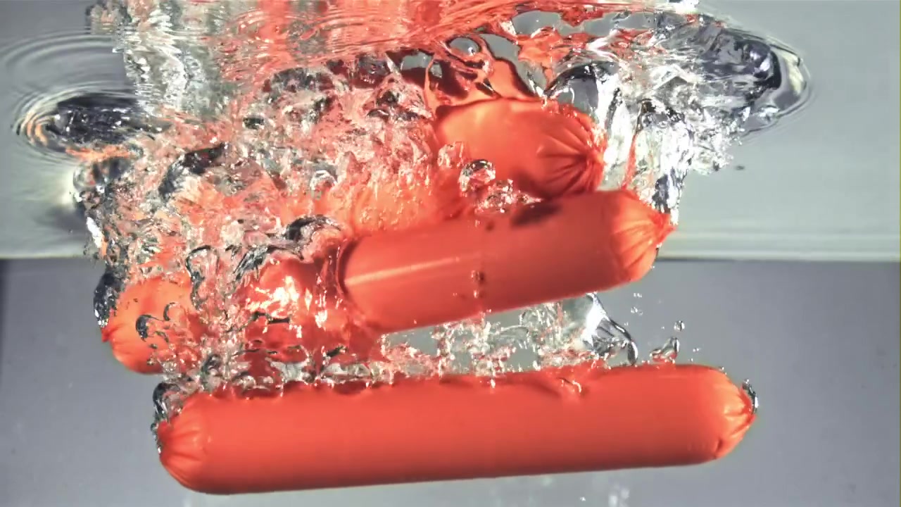 Hot dog che cadono al rallentatore nell'acqua con schizzi.